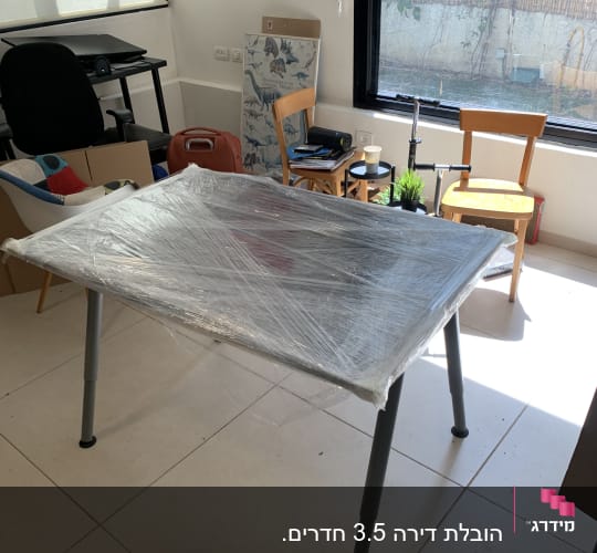 שולחן עטוף בניילון בחדר עם כיסאות וציוד ארוז